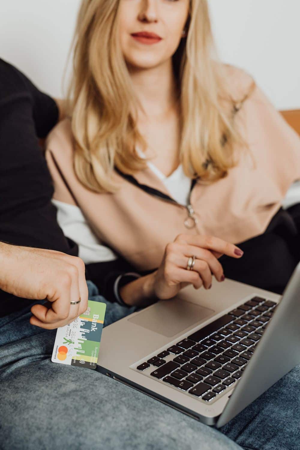 A woman holding a laptop while a man hands her a credit card, illustrating online shopping.
