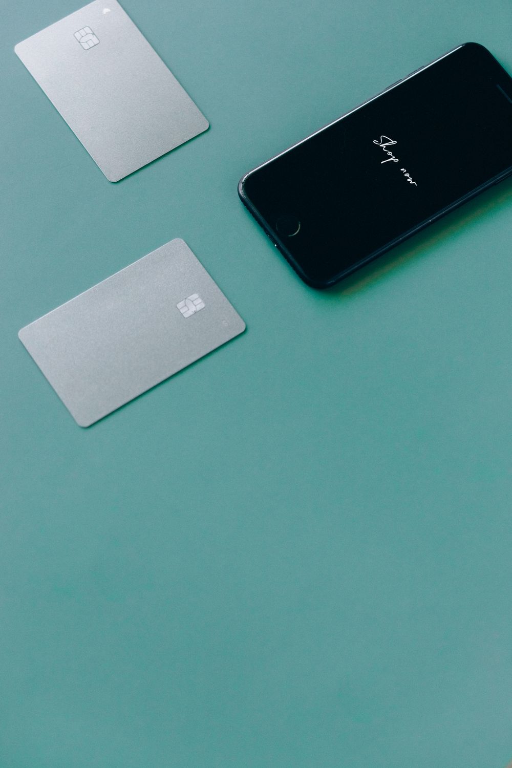 Two bank cards and a smartphone on a green surface, symbolizing online shopping.