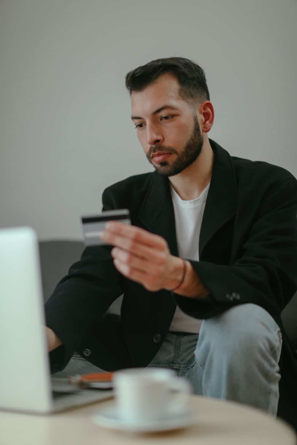 Man sitting indoors holding a credit card and using a laptop for online shopping.