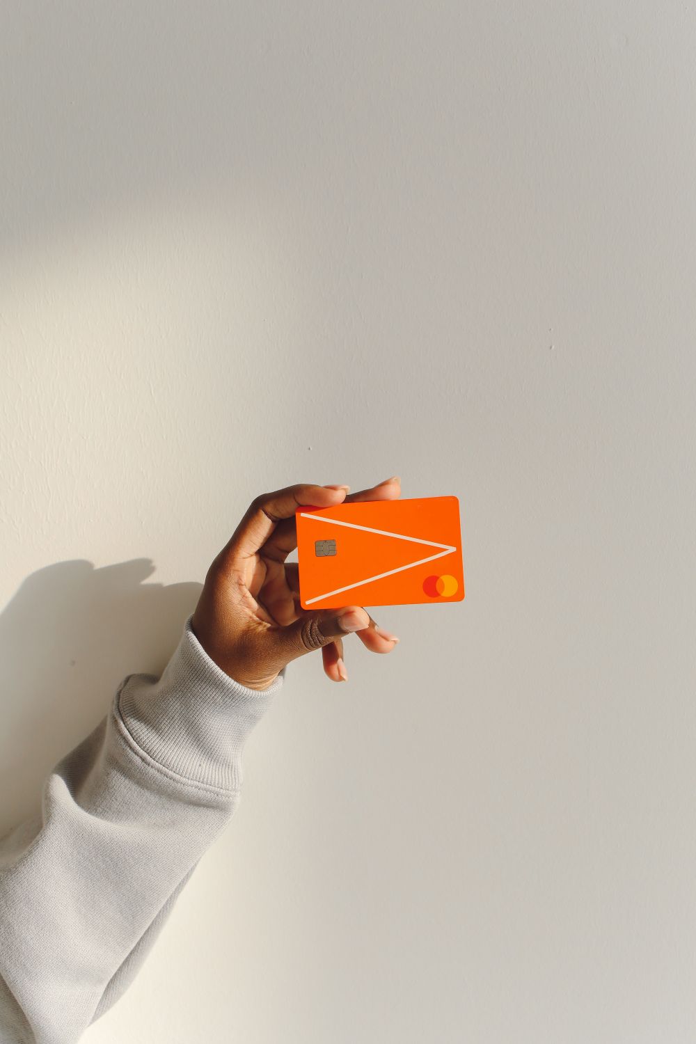 Close-up of a hand holding a bright orange debit card against a light background.