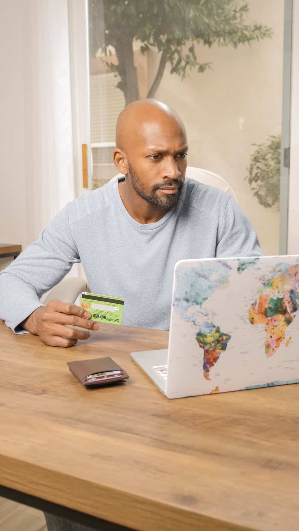Bald man using credit card for online shopping on colorful world map laptop indoors.