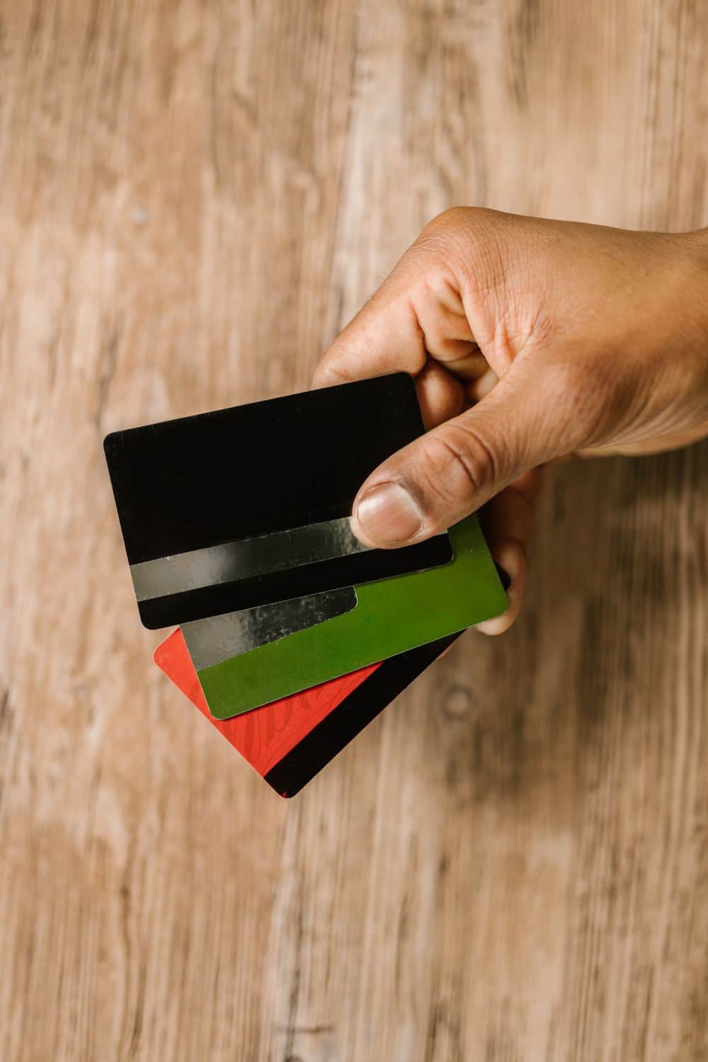 A hand holding multiple credit cards on a wooden background, emphasizing payment and finance themes.