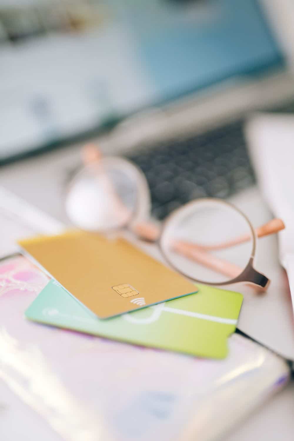 Blurred close-up of credit cards, eyeglasses, and laptop on a desk, evoking online shopping theme.