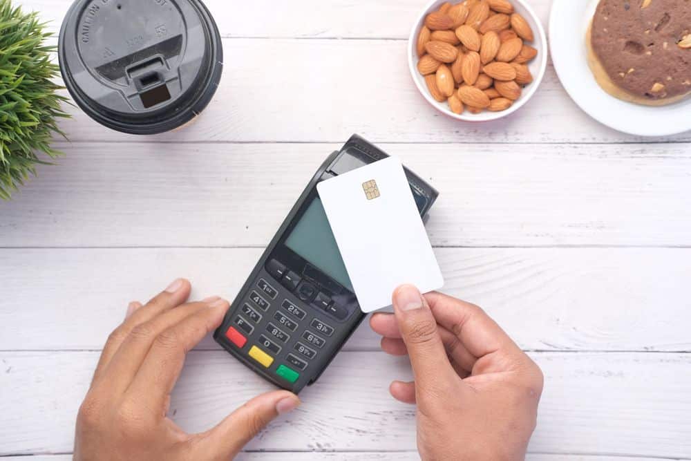 Hands making a contactless payment with a credit card on a wooden table.