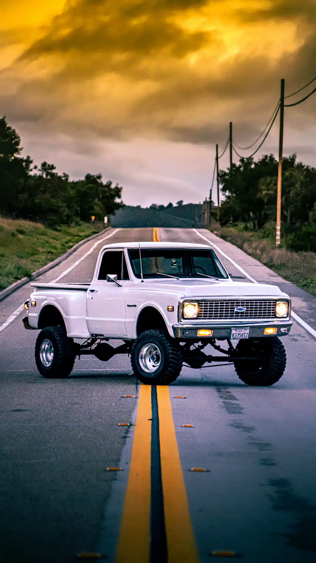 A white truck driving down a road under a cloudy sky