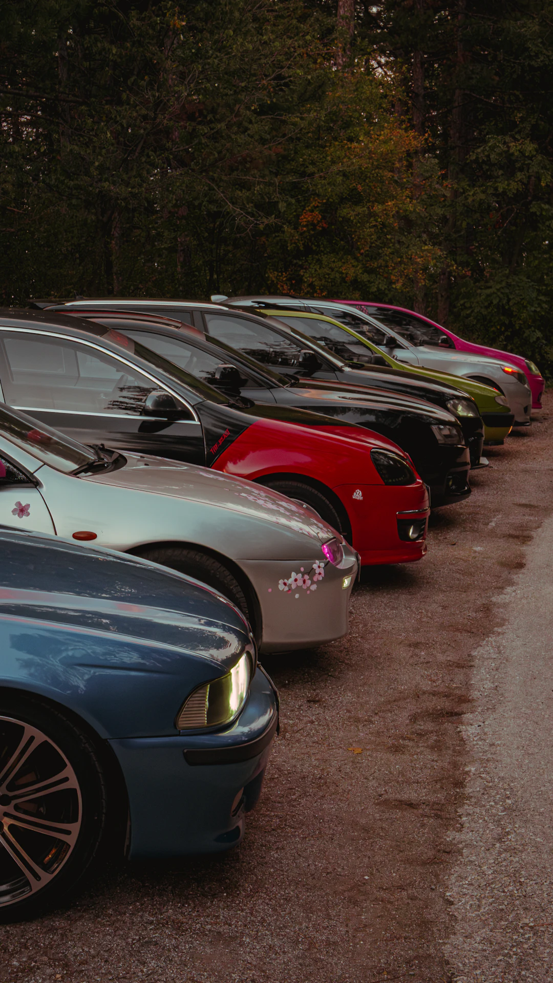 A line of custom cars parked on a dirt road.