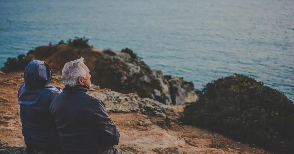two person sitting on rock staring at body of water during daytime
