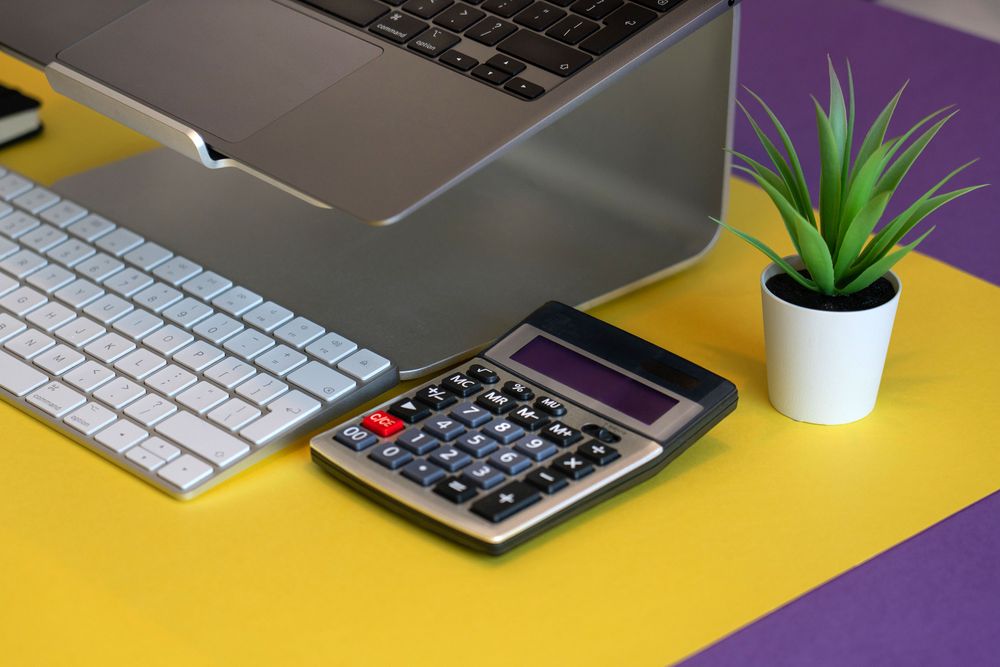 A stylish workspace featuring a laptop, calculator, and plant on a colorful background.