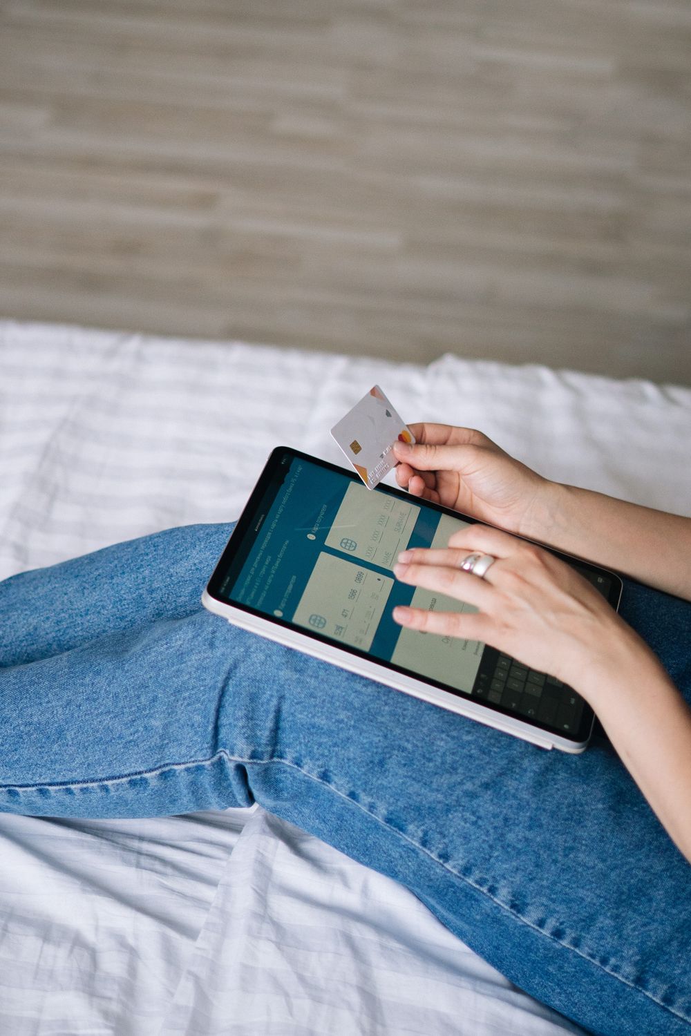 Person using a tablet and credit card for online shopping in a cozy home setting.