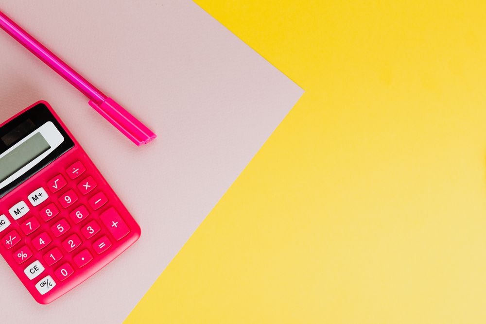 A vibrant pink calculator and pen on a yellow background, perfect for educational themes.