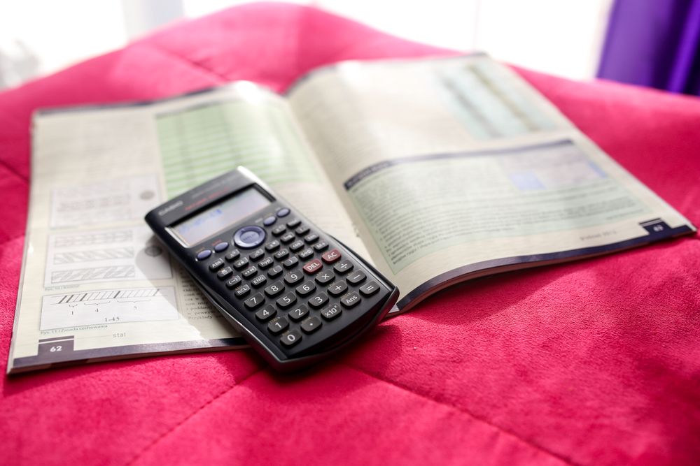 A scientific calculator and open textbook on a vibrant pink surface, ideal for education and academic themes.