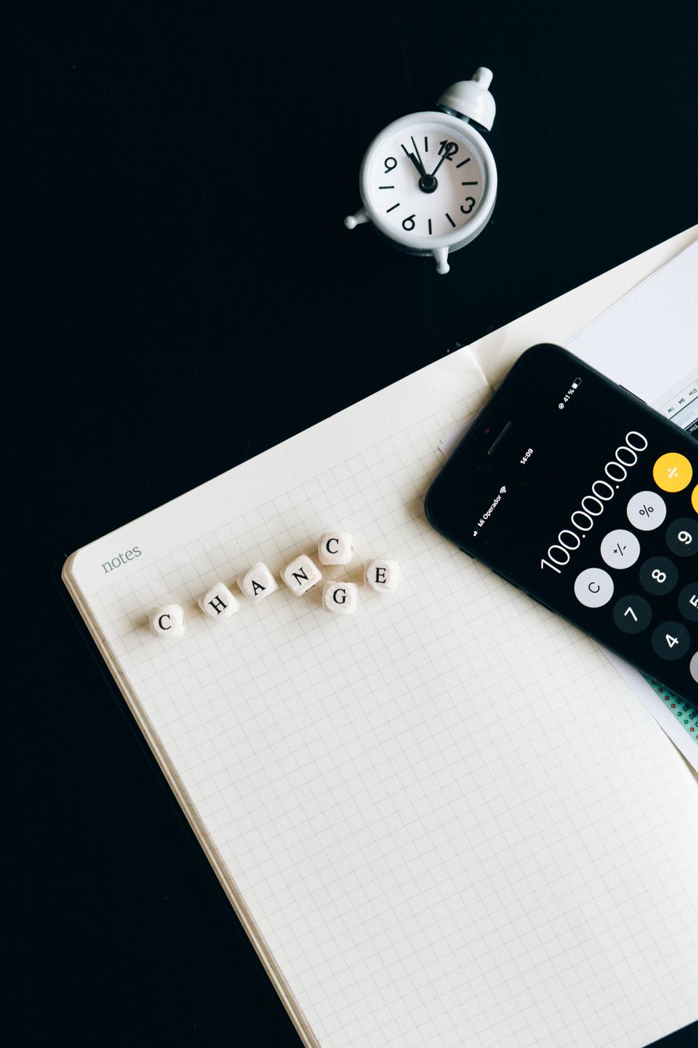 A creative still life featuring letter blocks spelling 'change', a clock, and a smartphone calculator.