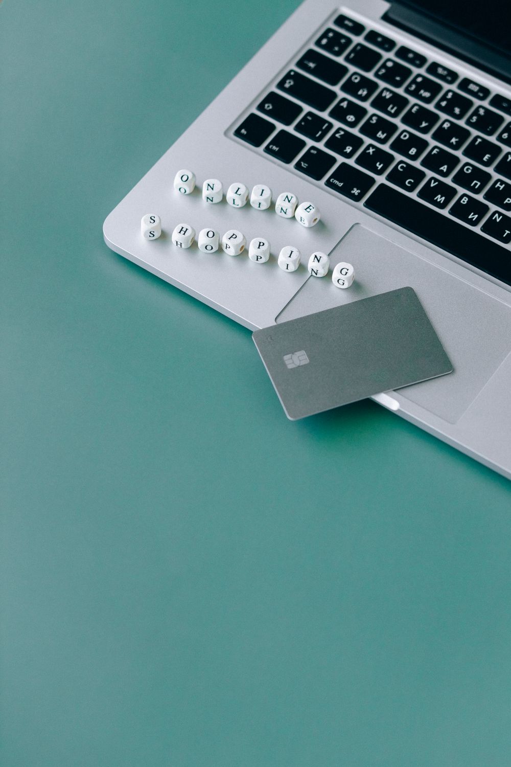 Minimalistic image of a laptop, bank card, and text spelling 'online shopping' on a green background.