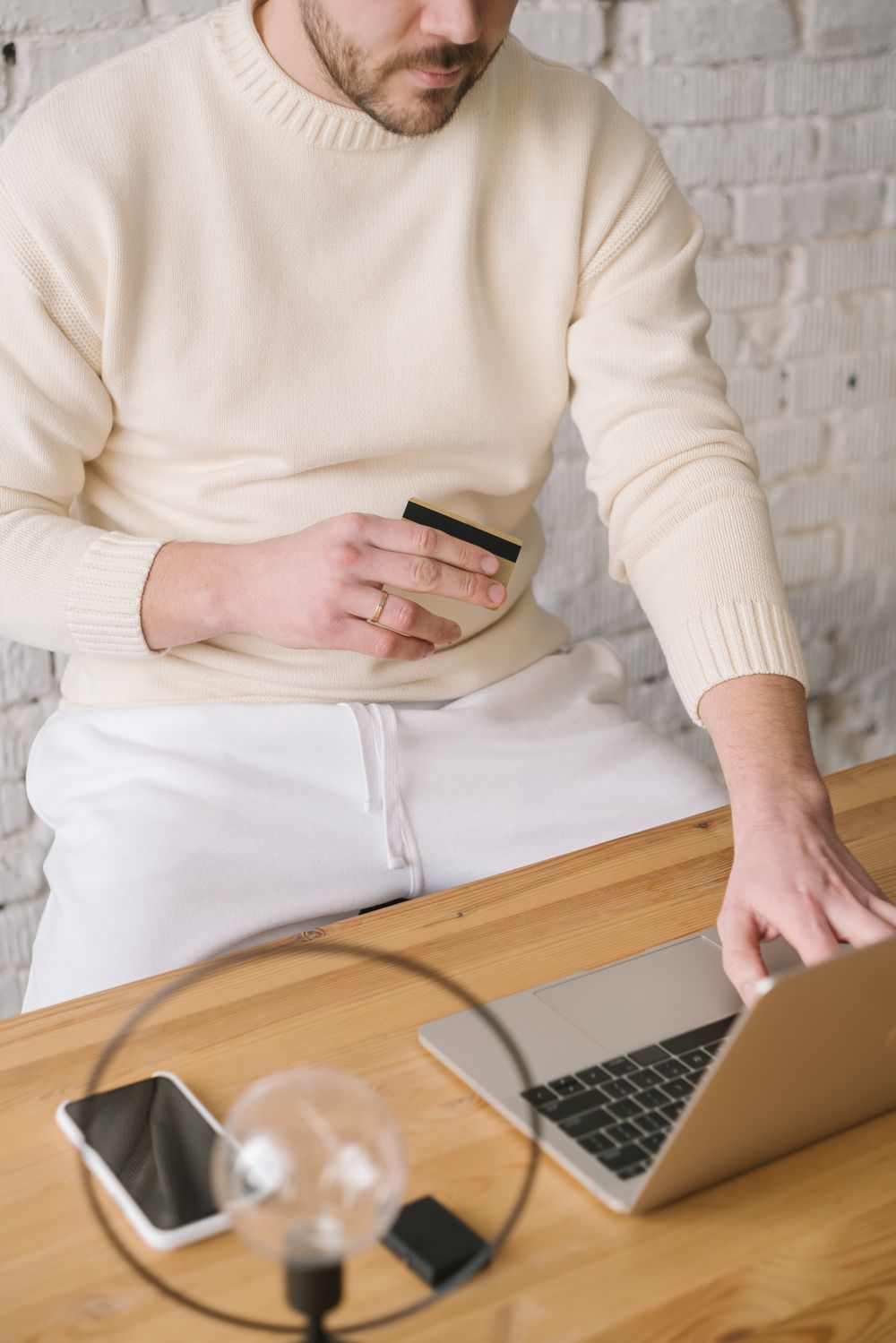 Adult man using laptop and holding credit card for online shopping in a minimalistic setting.