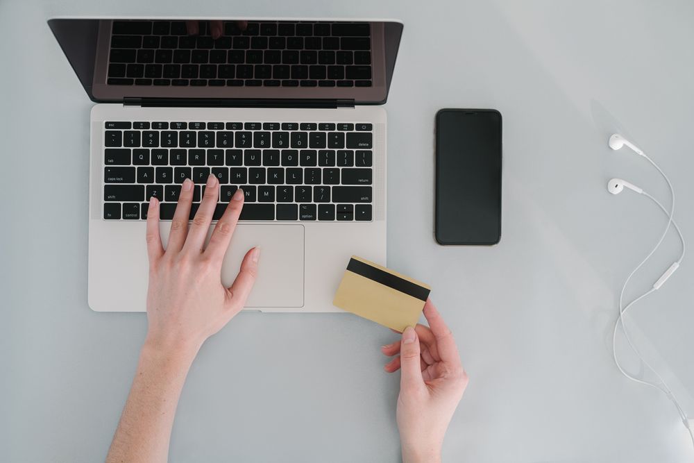 Flat lay of a workspace with a laptop, bank card, smartphone, and earphones, ideal for online finance themes.