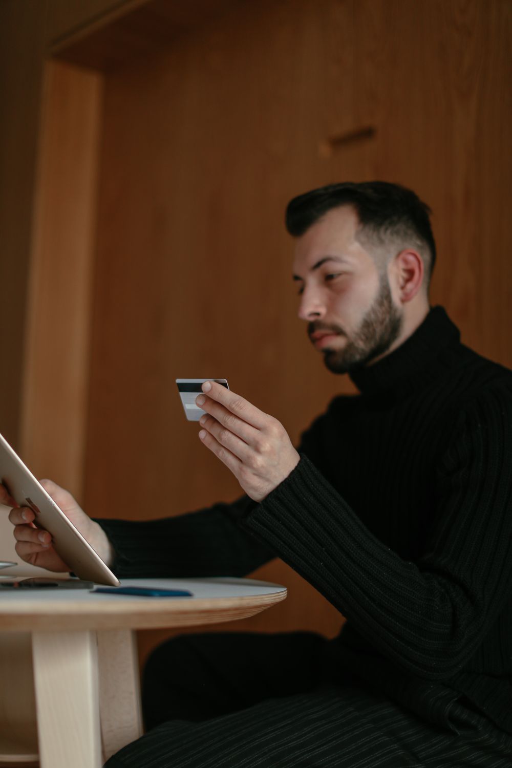Bearded adult man using a tablet and credit card for online shopping at home.