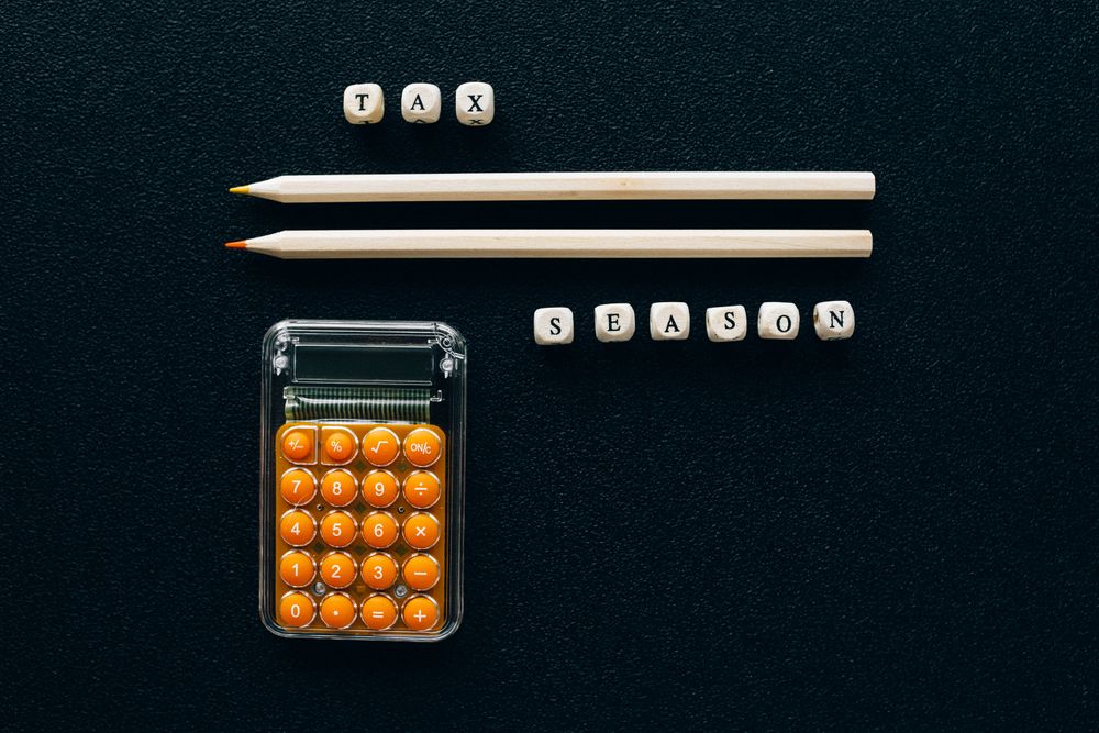 Top view of pencils, calculator, and letter blocks spelling 'tax season' on black background.