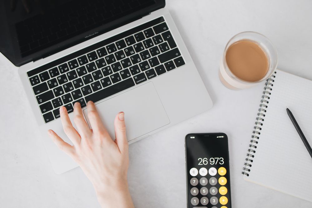 A person working on a laptop with a smartphone calculator and notebook nearby, ideal for business and technology themes.