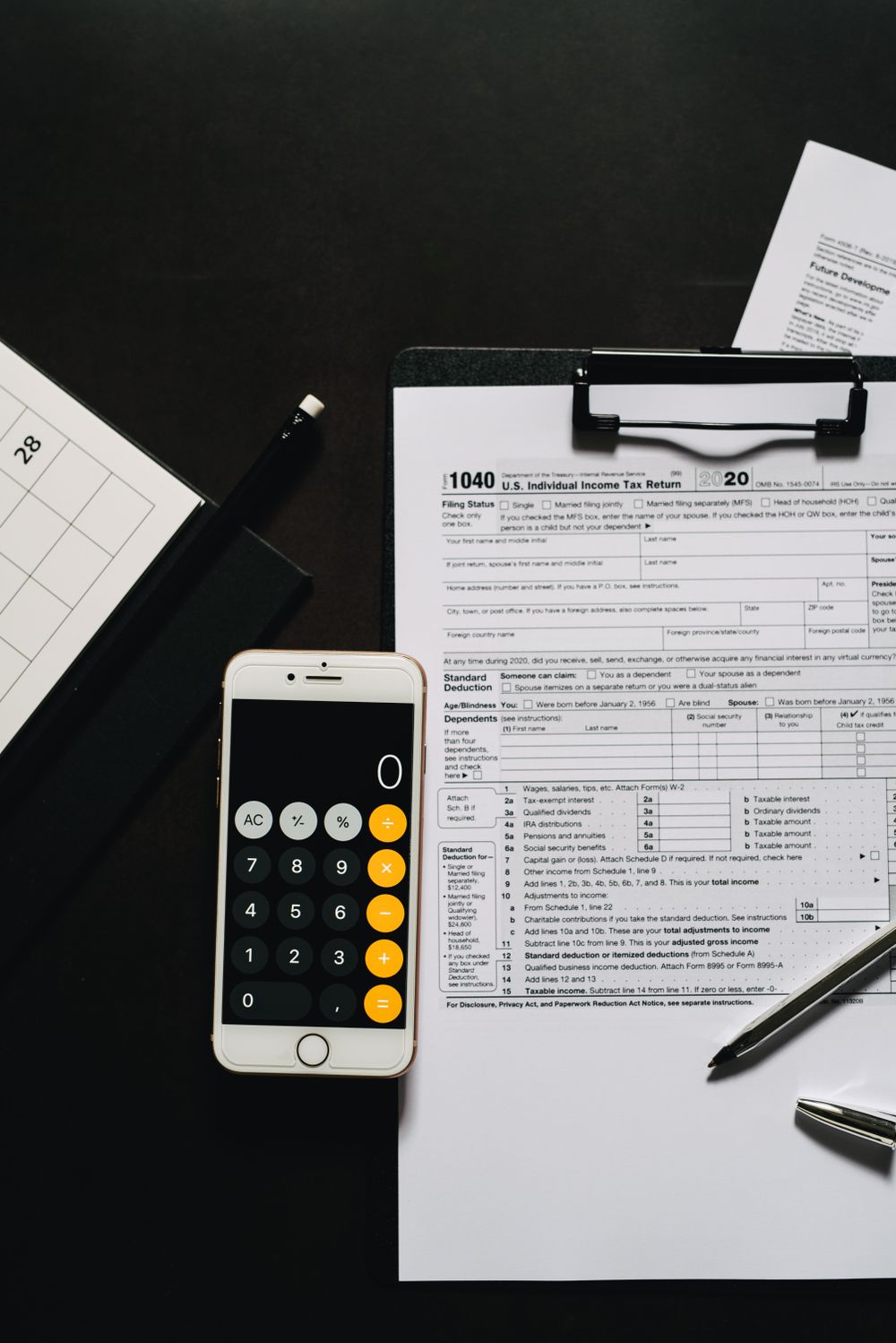 Overhead view of tax forms, a smartphone calculator, and clipboard for financial tasks.