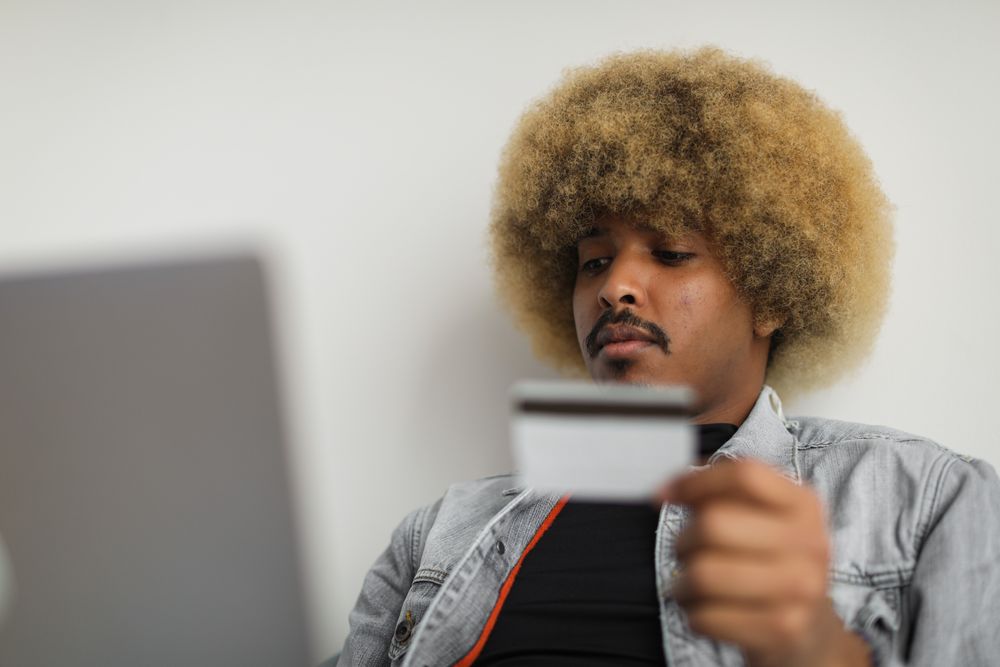 A man with afro hair on a laptop, holding a credit card for online shopping.