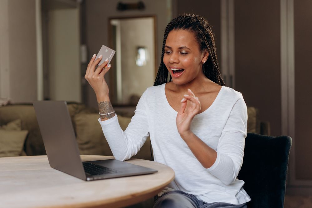 African American woman happily shopping online with a laptop and credit card.
