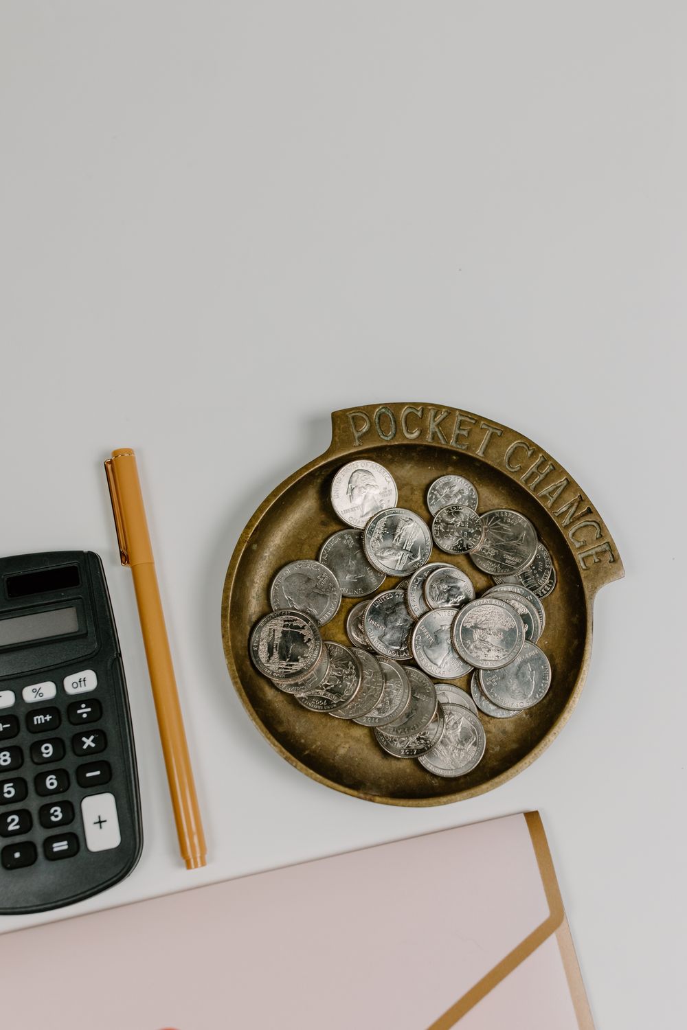Top-down view of coins, calculator, and pen on a white surface, ideal for finance concept.