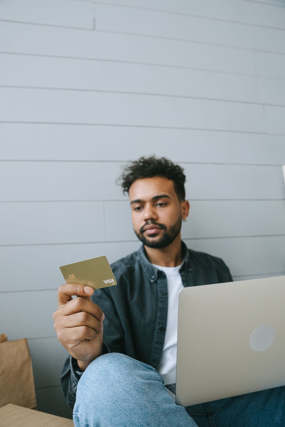 Man using Visa card for online shopping with laptop in a casual setting.