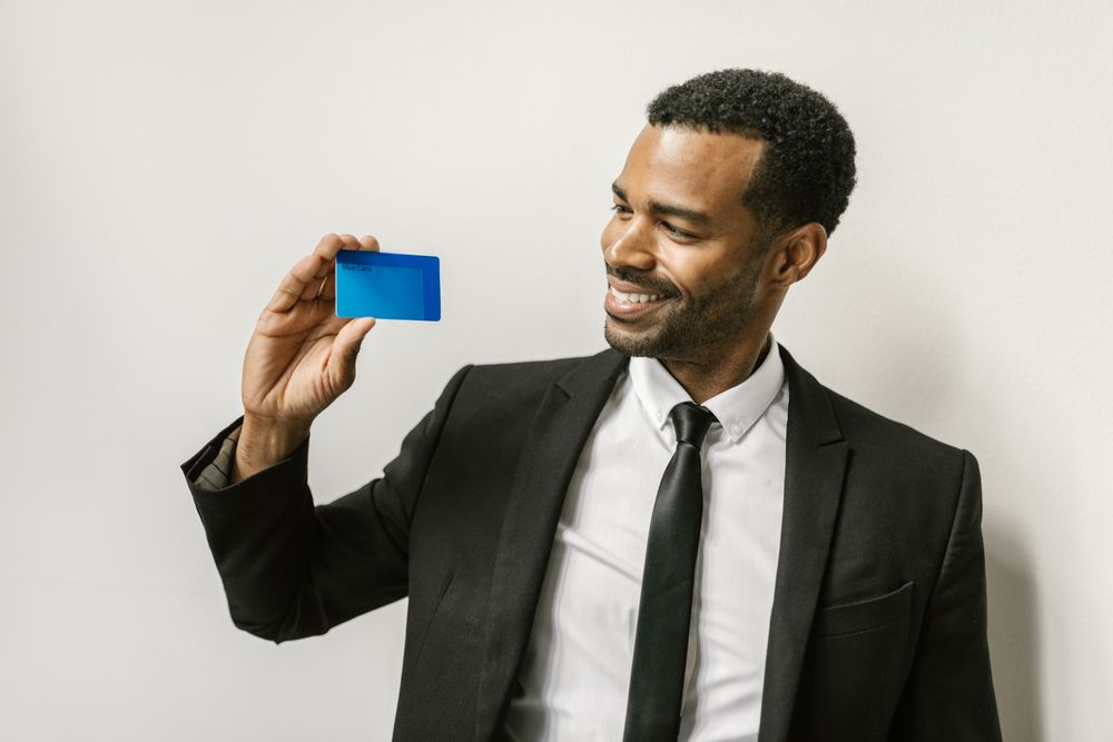 A confident man in a suit holds a credit card, smiling towards it.