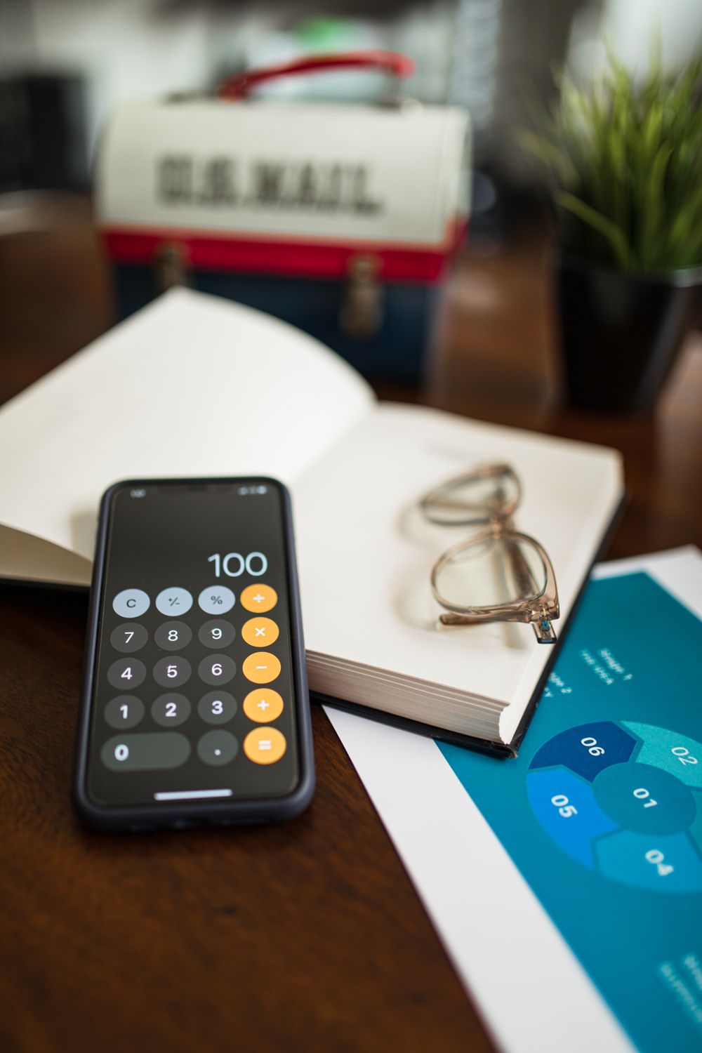 An organized desk with a smartphone calculator app, open book, and eyeglasses, ideal for productivity scenes.