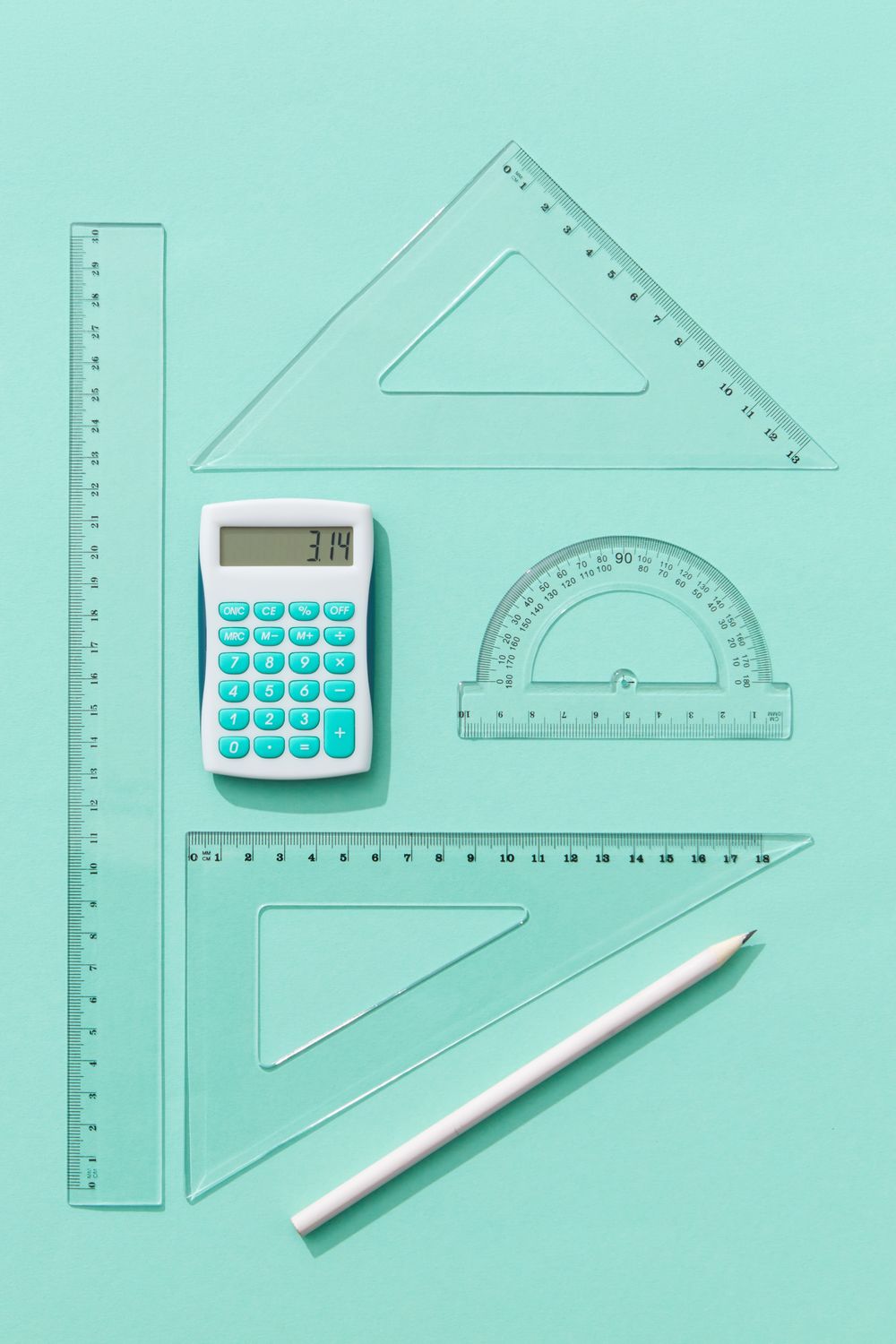 Flat lay of calculator, rulers, and protractor on teal background, ideal for educational concepts.