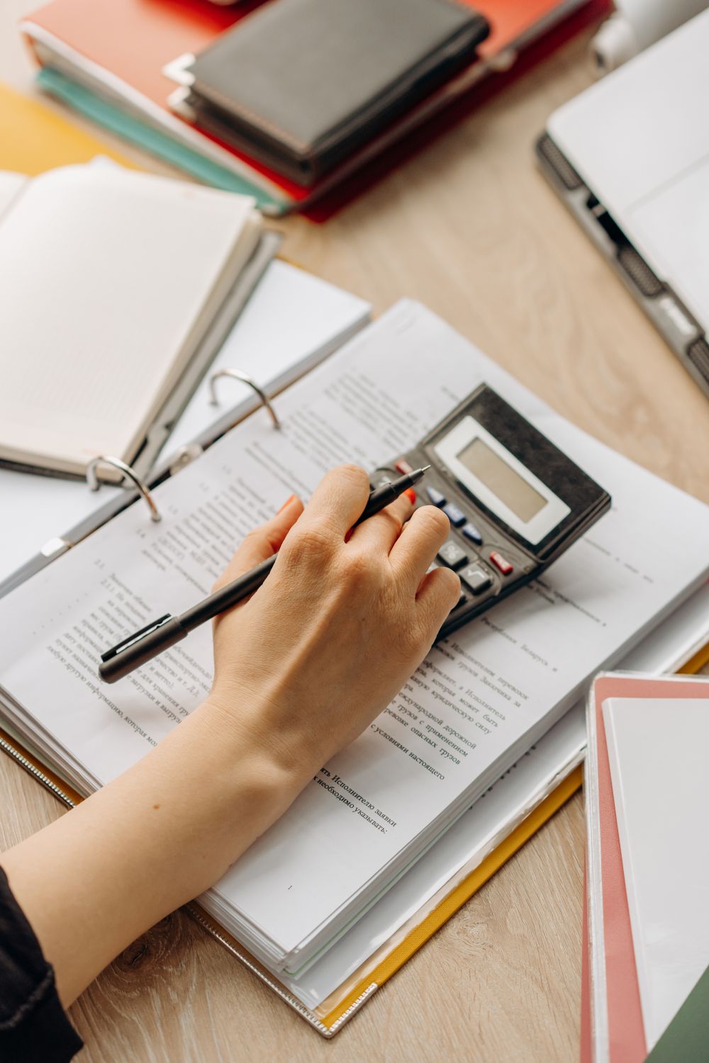 Close-up of a hand using a calculator on documents in an office setting.