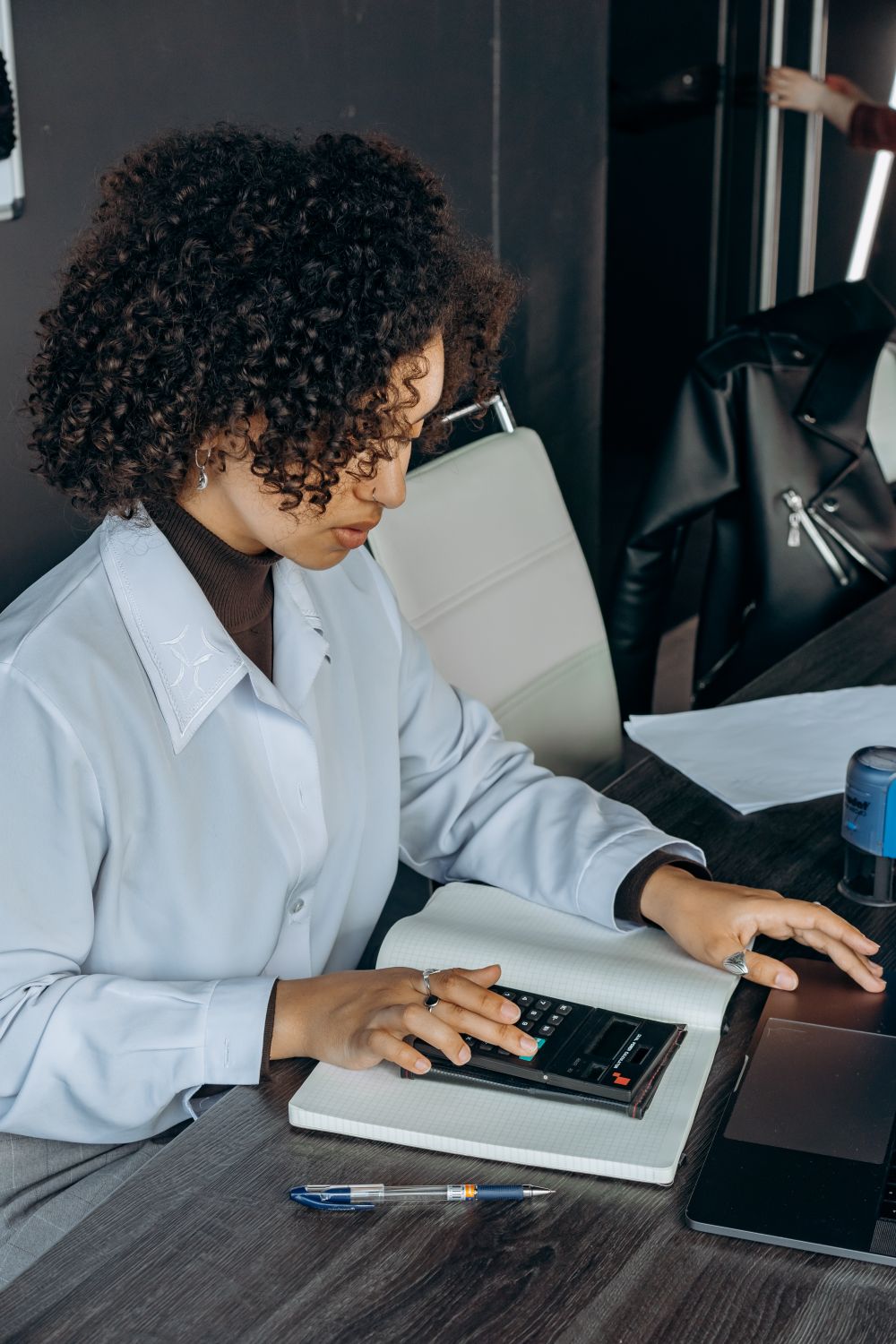 African American woman working on calculations at her desk using a calculator in a contemporary office setting.