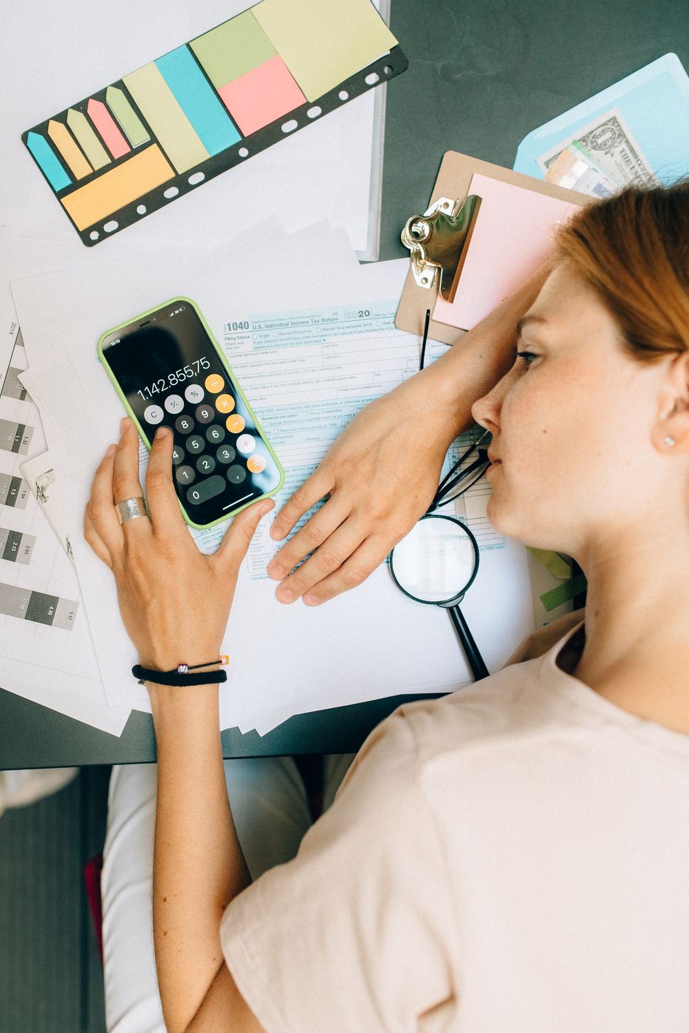 High-angle view of a woman calculating at her desk with documents and office supplies.