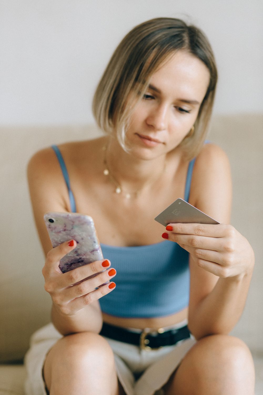 Young woman sitting indoors using her smartphone and a credit card for online shopping.