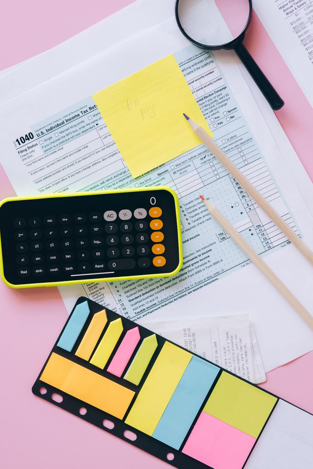 Office supplies including calculator, documents, and sticky notes on a pink surface.