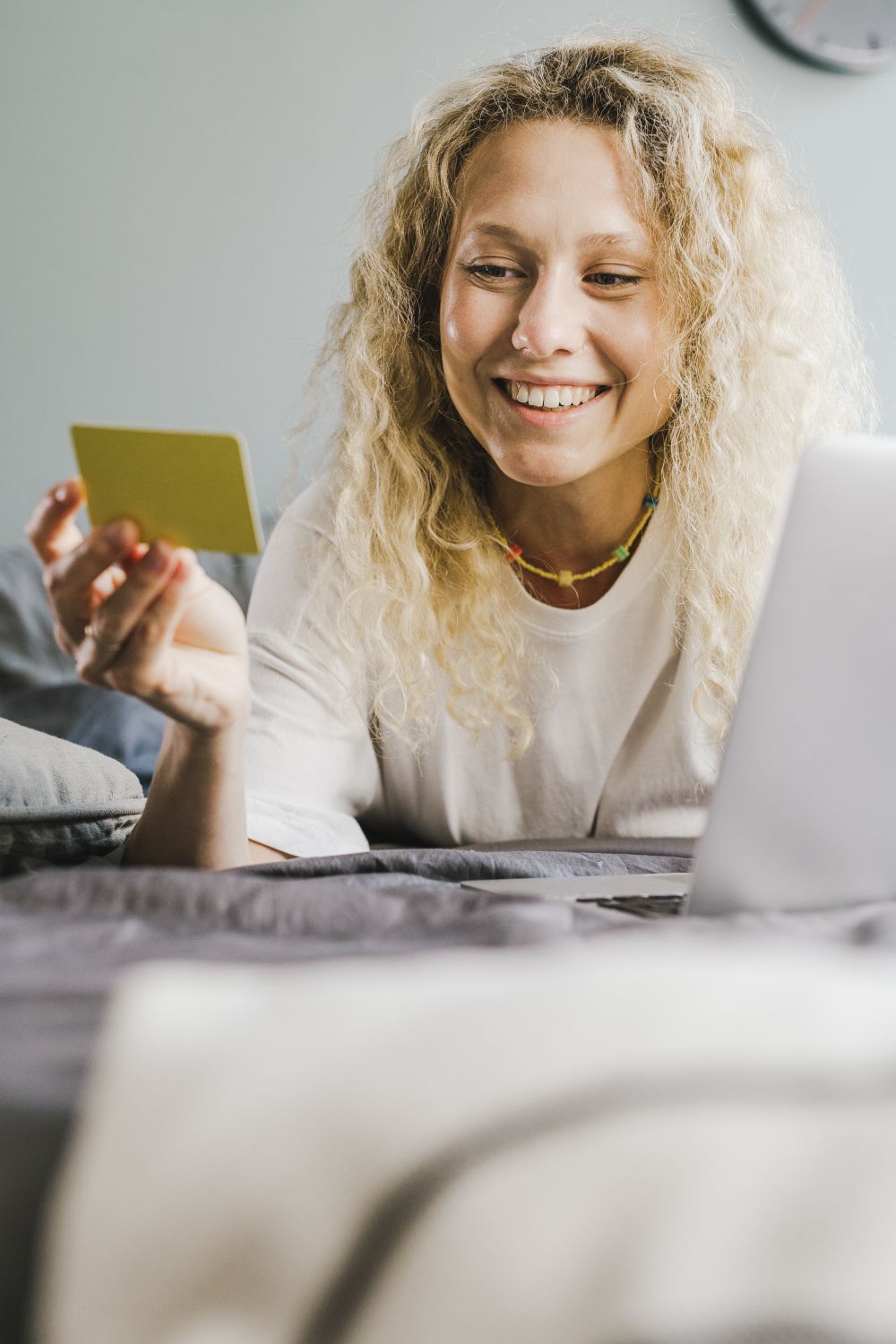 Blonde woman smiling while using a credit card and laptop indoors for online shopping.